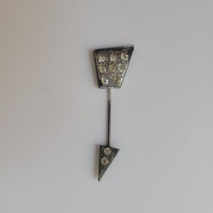 May include: A silver pin with a geometric design. The pin is decorated with clear rhinestones and has a pointed tip.