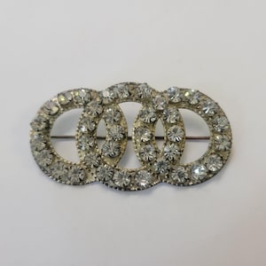 May include: A silver brooch with three interlocking circles, each circle is set with clear rhinestones.