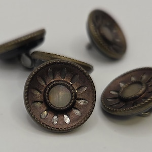 May include: Close-up of several antique bronze-colored buttons. Each button has a detailed floral design around a central, lighter-colored inset. The buttons are slightly raised and have a textured appearance, suggesting they are vintage or handcrafted.
