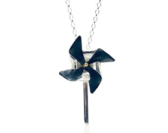 May include: A silver necklace with a black and silver pinwheel pendant. The pinwheel has a gold center.