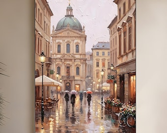 May include: An oil painting shows a European city street scene in the rain. The artwork features a large building with a green dome, cobblestone streets, and figures with umbrellas. The painting is displayed above a white sofa and a round wooden coffee table.
