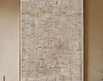 May include: A large, rectangular abstract painting with a textured, light beige surface, framed in gold, hangs above a modern living room. The room features a white sofa, wooden coffee table, and decorative vases, creating a neutral and inviting atmosphere.