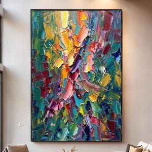 May include: Large abstract painting with a black frame. The artwork features bold brushstrokes in a vibrant array of colors, including yellow, red, green, and blue. The painting is displayed in a modern living room setting.