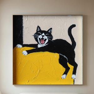 Könnte beinhalten: Gerahmtes Gemälde einer schwarz-weißen Katze, die gähnt. Die Katze liegt auf einer strukturierten gelben Oberfläche, mit einer schwarzen vertikalen Form auf der linken Seite. Der Hintergrund ist hellbeige.