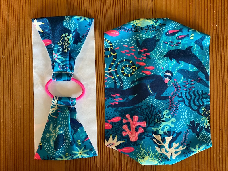 Puede incluir: Dos diademas de tela con fondo azul y una escena submarina colorida. Una diadema est&aacute; doblada y la otra est&aacute; plana. Ambas diademas tienen una banda el&aacute;stica rosa.