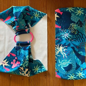 Puede incluir: Una diadema de tela azul y rosa con fondo blanco y un anillo rosa. La tela tiene un patr&oacute;n de peces, corales y otras criaturas marinas.