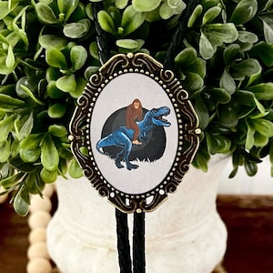 Bigfoot Bolo Tie for Men and Women, Bolo Ties with Big Foot Riding a Dinosaur T Rex, Yeti Hiking Sasquatch Gift for Boyfriend, Gift for Him