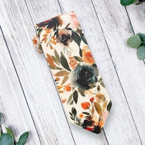 May include: A cream-colored tie with a floral pattern featuring watercolor-style flowers in shades of orange, pink, green, and blue.