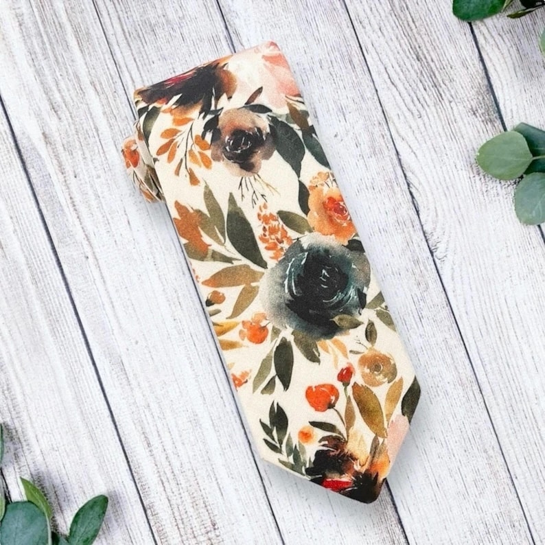 May include: A cream-colored tie with a floral pattern featuring watercolor-style flowers in shades of orange, pink, green, and blue.