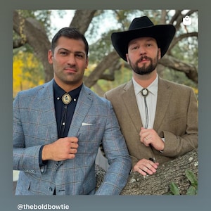Puede incluir: Dos hombres con trajes y corbatas bolo. Uno lleva una blazer a cuadros azul, una camisa negra y una corbata bolo con un emblema dorado. El otro lleva una blazer marr&oacute;n, un sombrero de vaquero negro y una corbata bolo con un dise&ntilde;o de flor blanca.