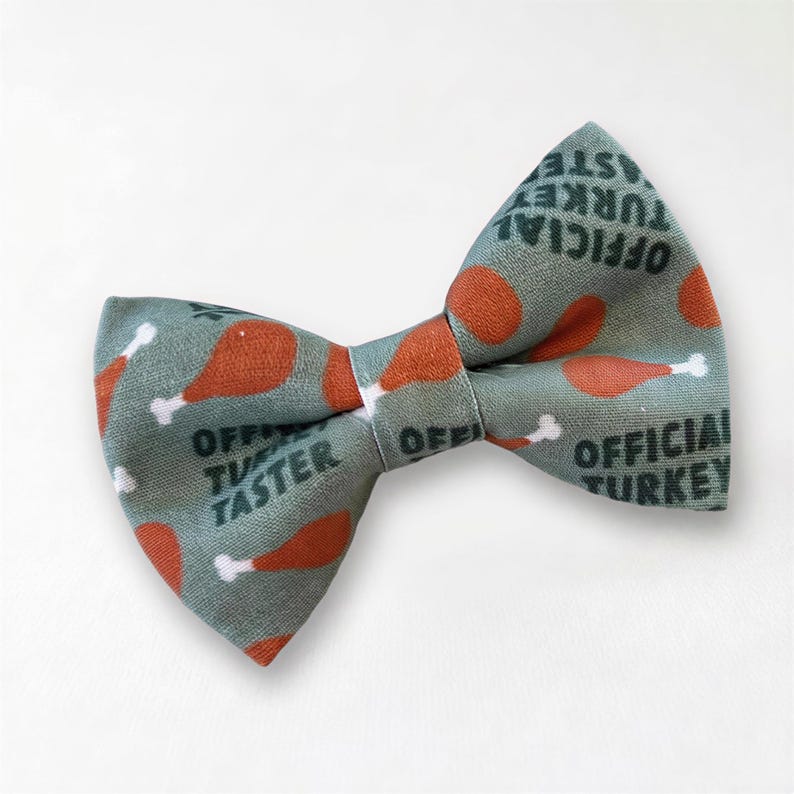 A Thanksgiving cat bow tie with a pattern of orange and white turkey images, along with the text "OFFICIAL TASTER" printed on it.