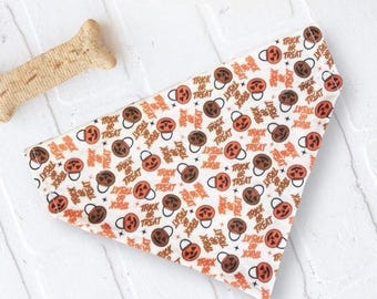 May include: A triangular pet bandana featuring a white background with a repeating pattern of orange jack-o'-lantern candy buckets and the text Trick or Treat printed in black. The fabric accessory has a folded top edge.