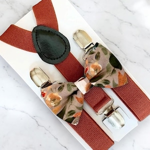 May include: A set of burnt orange suspenders and a bow tie with a floral pattern. The bow tie has a light brown background with orange, yellow, and green flowers.