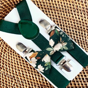 May include: A set of green suspenders and a bow tie with a floral pattern. The bow tie has white flowers and green leaves on a dark green background.
