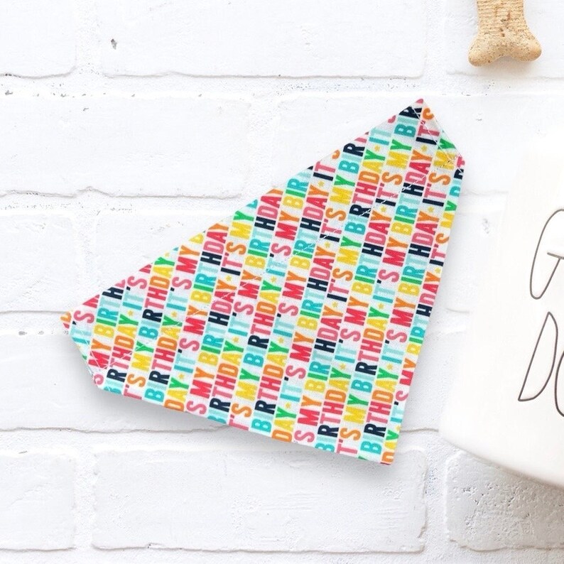 May include: A white bandana with a colorful repeating pattern of the text "It's My Birthday".