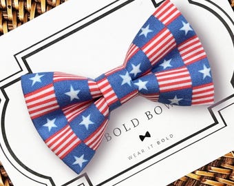 Pode incluir: Uma gravata borboleta com um padrão repetitivo de estrelas brancas sobre fundo azul e listras vermelhas e brancas. A gravata borboleta é exibida em um cartão branco com o texto BOLD BOW e WEAR IT BOLD impresso em preto com um ícone.