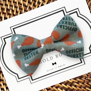 A Thanksgiving dog bow tie with a pattern of orange and green turkey images is displayed on a white card with text.