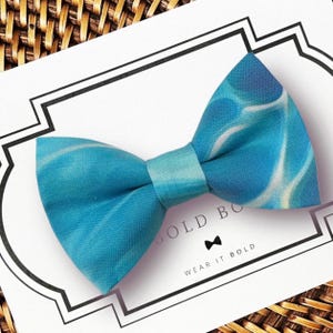 May include: A blue bow tie with a white and blue marbled pattern. The bow tie is on a white card with the text "BOLD BOW" and "WEAR IT BOLD". The bow tie is made of fabric.