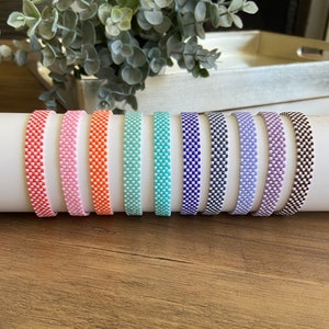 May include: A set of ten colorful bracelets with a checkered pattern. The bracelets are made of small beads and are all different colors, including orange, pink, blue, turquoise, purple, and brown.