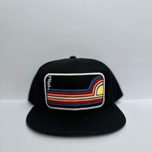 May include: Black baseball cap with a colorful sunset graphic patch on the front. The patch has a white border and the text "MTZL" is written in white on the patch.