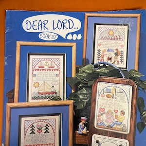 May include: A book cover for a cross-stitch pattern book titled "Dear Lord... Book 57". The cover features four framed cross-stitch designs with religious themes. The designs include a sailboat, a family, a house, and a calendar with the month of July.