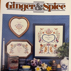 May include: A cross-stitch pattern booklet with the title "Ginger & Spice" and the text "Folk Art Announcement". The booklet features three cross-stitch designs, including a heart-shaped design with the text "Wed Today", a square design with the text "Baby's Name", and an octagonal design with the text "Wed Today Names".