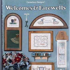 May include: A page from "Canterbury Designs" featuring cross-stitch patterns with the title "Welcomes & Farewells." The designs include framed samplers with ducks, houses, and inspirational quotes. A floral arrangement and decorative shelf are also visible.