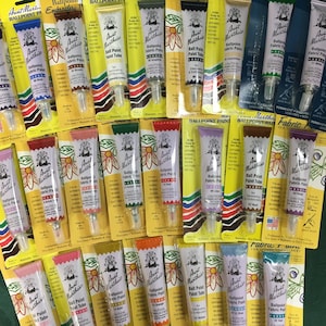 May include: A collection of 30 Aunt Martha's Ballpoint Fabric Paint tubes in various colors. The tubes are labeled with the color name and have a caution label. The paint is permanent, washable, and lead-free.
