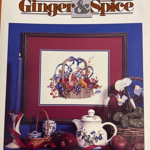 May include: A cross-stitch pattern booklet titled "Bountiful Basket" by Ginger & Spice. The cover features a framed image of a basket overflowing with fruit and flowers, surrounded by a blue background and a still life of a teapot, apples, and candles.