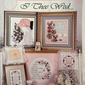 May include: A collection of framed counted cross-stitch samplers with wedding themes. The samplers feature floral designs, wedding rings, and romantic quotes. The color palette includes pink, white, and gold.