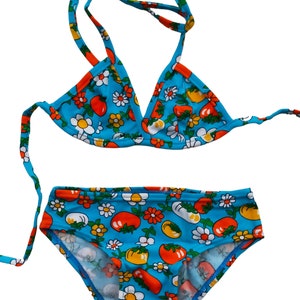 Può includere: Un bikini blu con stampa floreale con pomodori rossi e fiori bianchi. La parte superiore del bikini è di stile triangolare con spalline regolabili. La parte inferiore del bikini è di stile vita alta.