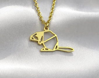 May include: A gold-coloured necklace with a geometric beaver pendant. The pendant is a stylised outline of the animal, with a chain of small, linked circles. The necklace is displayed on a white, textured surface.