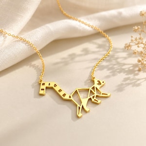 Gold-plated origami lemur necklace on cream fabric, geometric ring-tailed lemur pendant on a fine chain