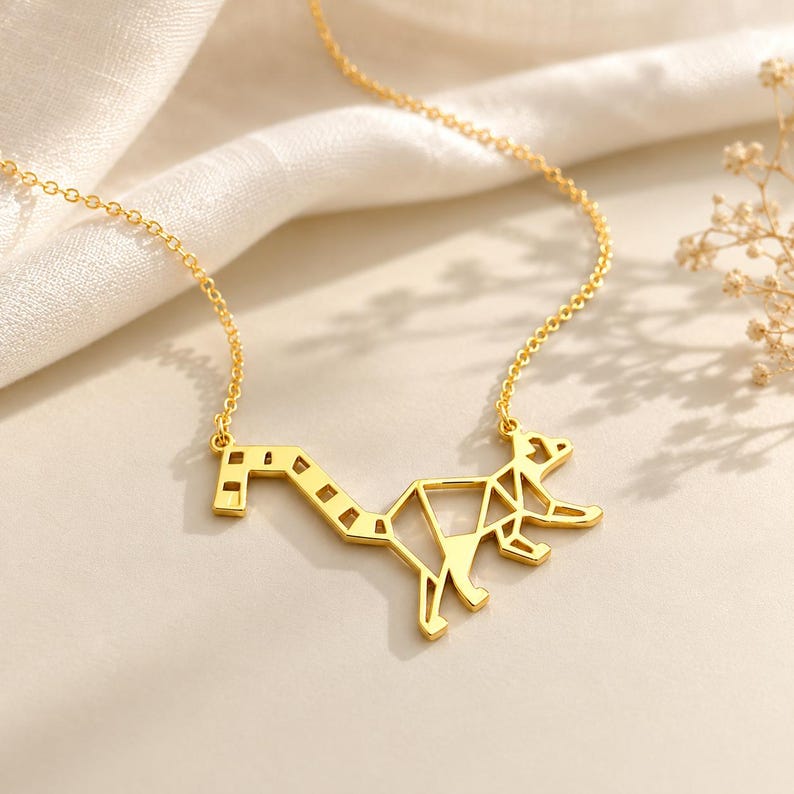 Gold-plated origami lemur necklace on cream fabric, geometric ring-tailed lemur pendant on a fine chain