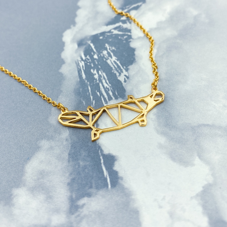 Peut inclure: Un collier en or avec un pendentif en forme d'hippopotame g&eacute;om&eacute;trique. Le pendentif est fait de m&eacute;tal fin et pr&eacute;sente un design d&eacute;licat et complexe.