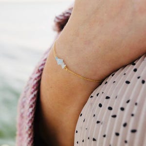 Op de afbeelding: Een delicate gouden kettingarmband met kleine, lichtblauwe edelsteenaccenten.