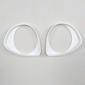 May include: Two white plastic cookie cutters shaped like eyes. The cutters are about 3 inches long and 2 inches wide.