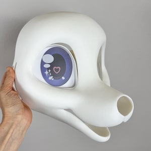 May include: A white, cartoon-style animal head with large, expressive eyes. The eyes feature a purple iris with a pink heart and stars. The head has a rounded shape with a snout and open mouth, suggesting a costume or mask.