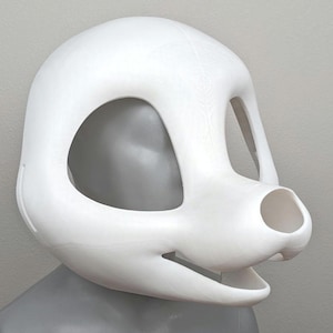 May include: A white, blank fursuit head base with large eye openings, a snout, and a mouth opening. The head is smooth and rounded, with a neutral expression. The base is designed for customization.