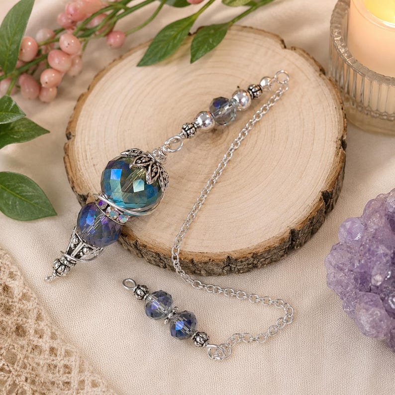 May include: A pendulum featuring a large, faceted, iridescent blue and teal crystal bead topped with silver filigree metalwork. The chain is made of silver-toned metal links and is accented with smaller, matching blue crystal beads and silver spacers.