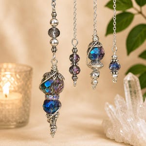 May include: Four silver-toned metal pendulums hanging from chains, each featuring faceted dark blue and iridescent crystal beads. The designs incorporate intricate wire wrapping, small silver spacer beads, and decorative metal caps, creating a vertical arrangement of dangling ornaments.