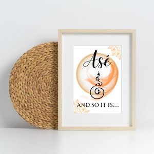 Op de afbeelding: Een ingelijst afdruk met een witte achtergrond en een perzikkleurige cirkel met het woord "Asé" in zwarte schrijfletters. De cirkel bevat een zwart symbool. De tekst "AND SO IT IS..." staat onder de cirkel.