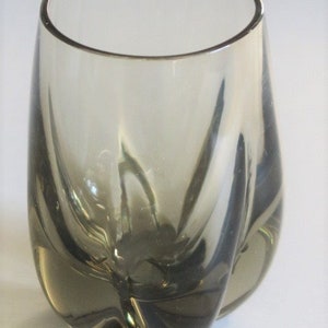 May include: A clear glass vase with a unique, organic shape. The vase has a dark gray tint and a rounded bottom.