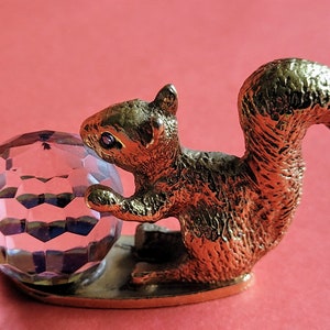 May include: A gold-colored squirrel figurine holding a clear crystal ball. The squirrel has a detailed textured surface and a purple eye.