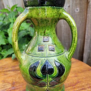 May include: A green ceramic vase with two handles and black geometric designs. The vase has a glossy finish and a slightly textured surface.