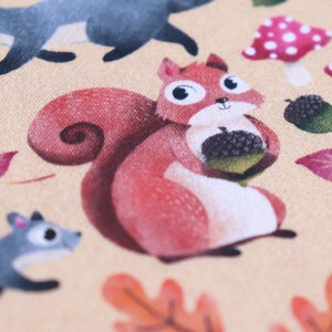 May include: A red squirrel with a bushy tail holds an acorn in its paws. The squirrel is sitting on a beige background with a brown leaf and a mushroom with white polka dots.