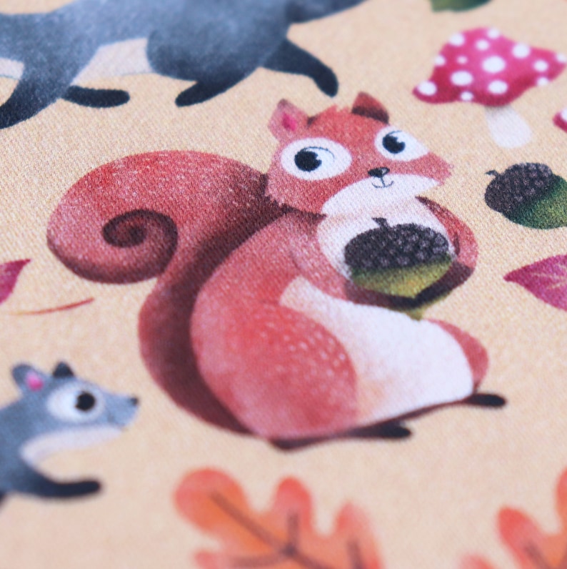 May include: A red squirrel with a bushy tail holds an acorn in its paws. The squirrel is sitting on a beige background with a brown leaf and a mushroom with white polka dots.