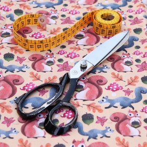 May include: A fabric with a repeating pattern of squirrels, mushrooms, and leaves. A silver pair of fabric shears and a yellow measuring tape are on top of the fabric.