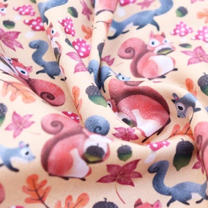 May include: A beige fabric with a repeating pattern of squirrels, acorns, and leaves. The squirrels are red and brown with bushy tails. The leaves are in shades of red, orange, and yellow. The acorns are brown.