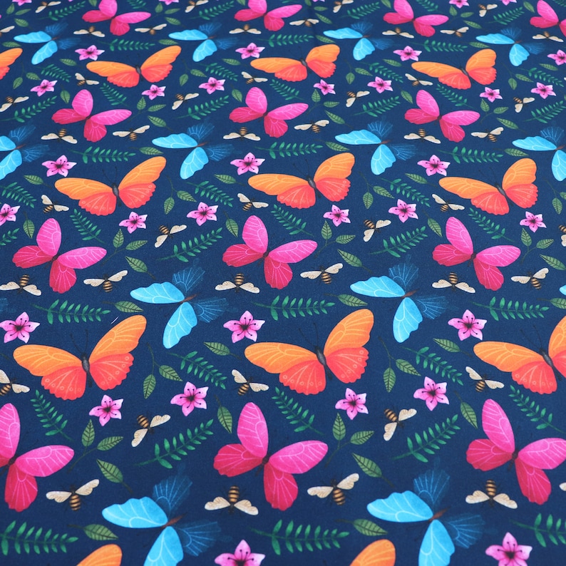 May include: A seamless fabric pattern featuring a repeating design of colorful butterflies on a dark blue background. The butterflies are in shades of pink, orange, and blue, and are arranged in a symmetrical pattern.